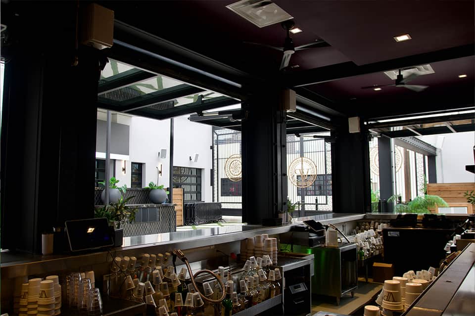 Contemporary coffee bar with black counters, shelving, and glass doors opening to courtyard