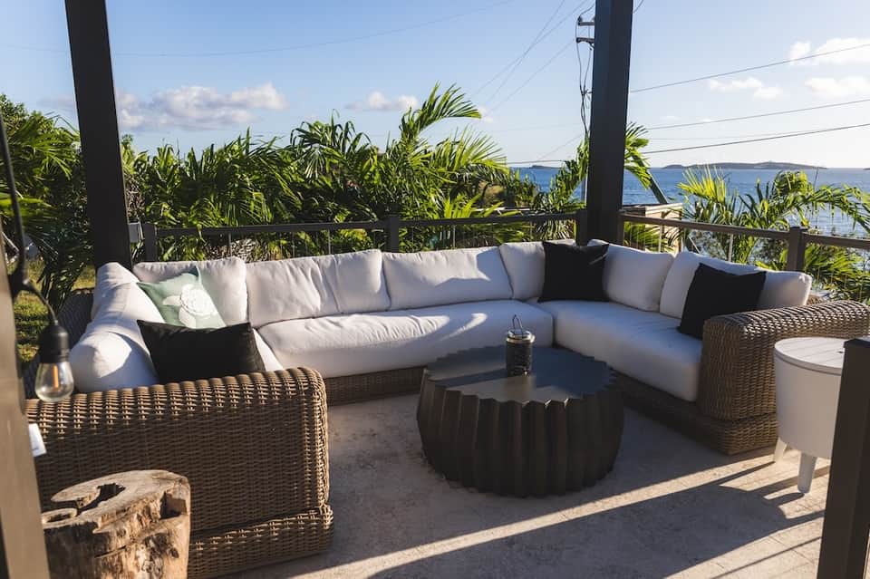Waterfront sectional sofa seating on deck with wicker furniture, tropical plants, and water view
