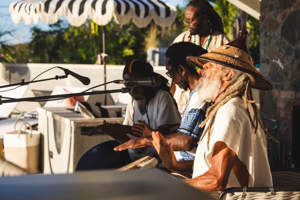 Musicians performing at an outdoor poolside event under a striped umbrella