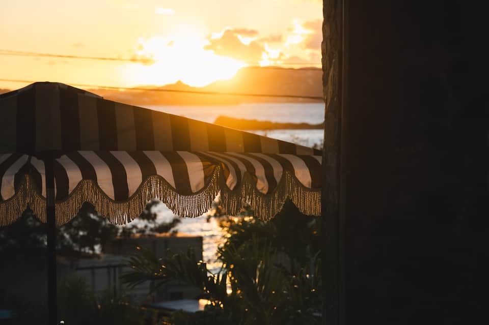Sunset view through striped awning over water with mountains, golden hour lighting, tropical setting