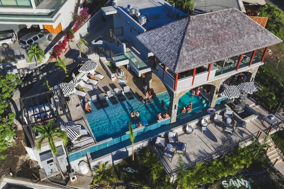 Aerial view of resort pool with striped umbrellas, pavilion structures, and surrounding landscaping
