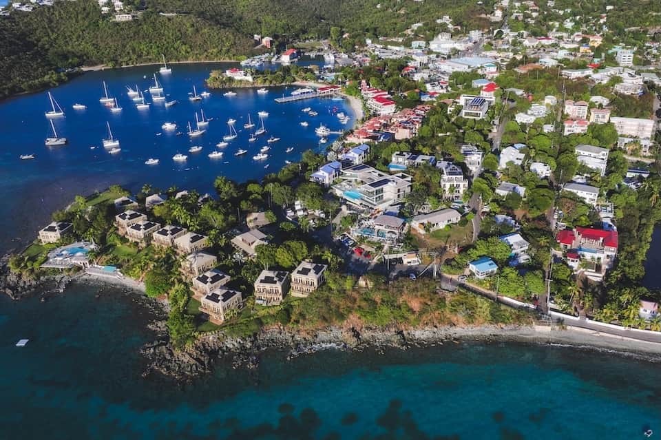 Aerial view of coastal waterfront community with sailboats, houses, and rocky shoreline along blue water