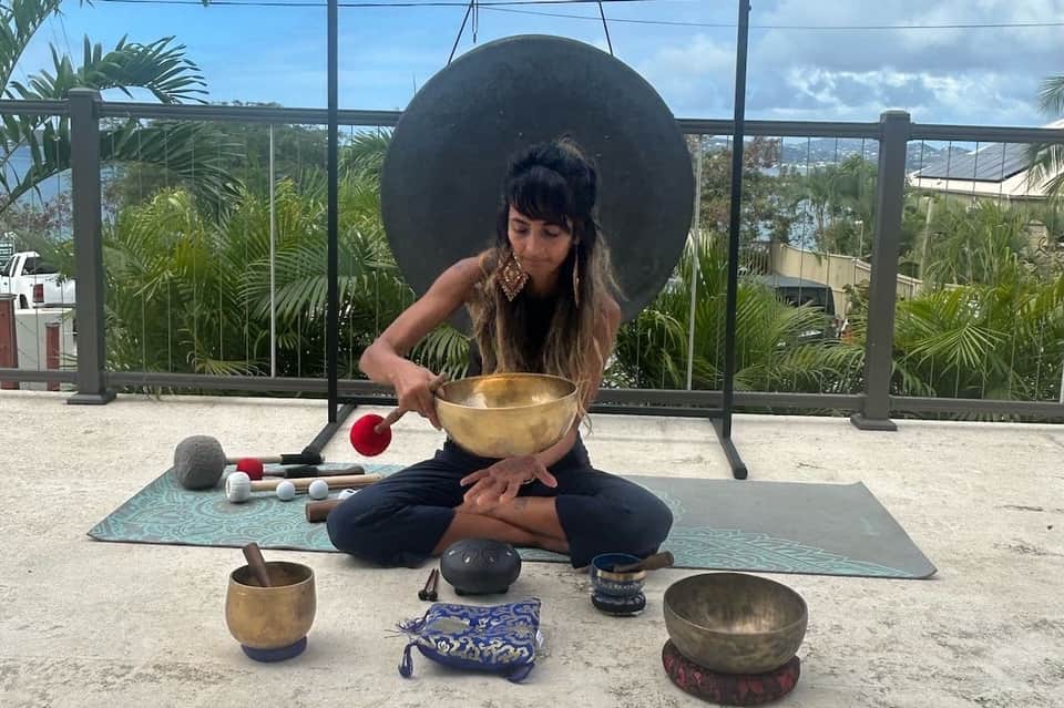 Woman meditating with singing bowl on mat overlooking tropical landscape