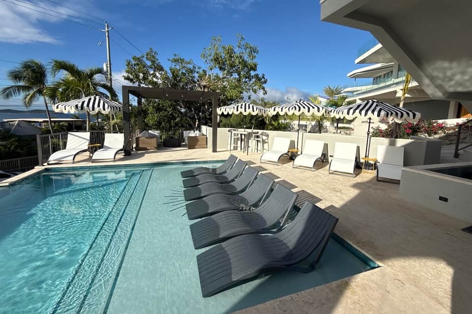 Contemporary resort pool with striped awnings, lounge chairs, and coastal landscape views