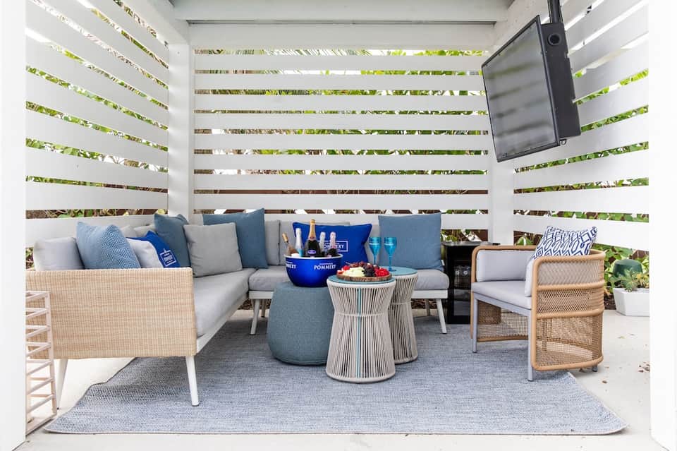 Private patio seating area with slatted fence, cushioned furniture, and hanging television