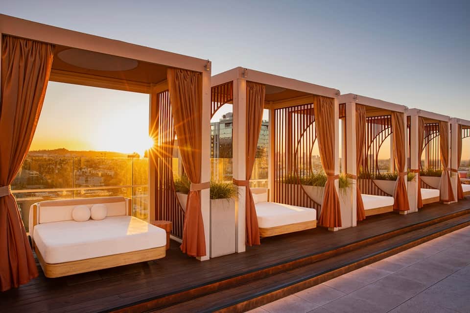 Rooftop cabanas with copper-colored frames and white bedding at sunset with city views