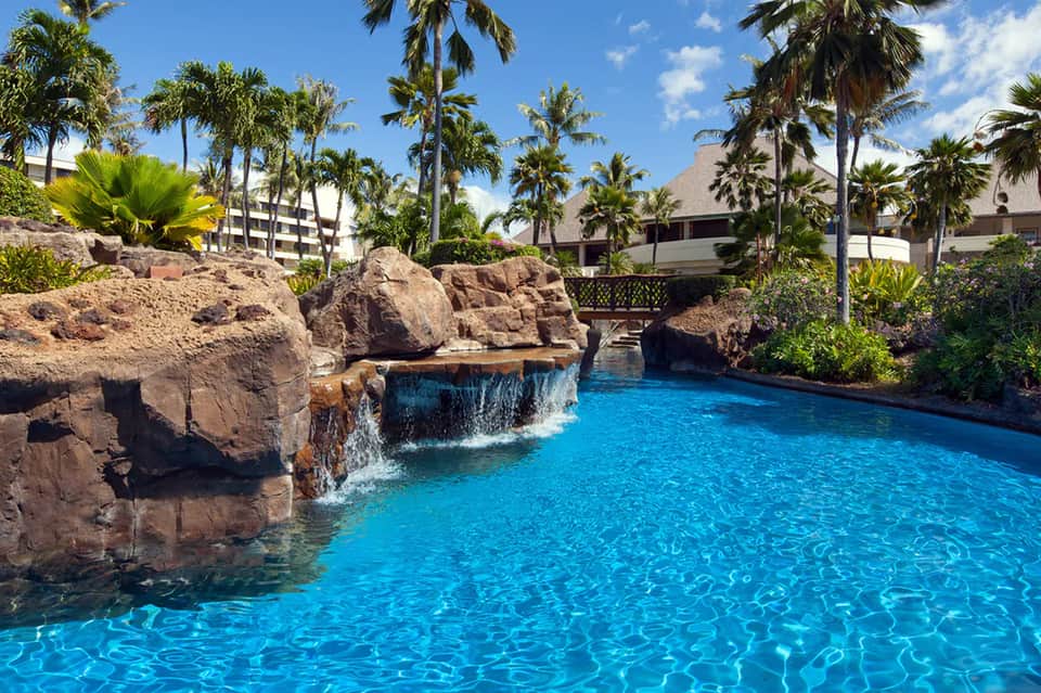 Resort lazy river with rock features, waterfalls, and tropical palm trees surrounding crystal blue water