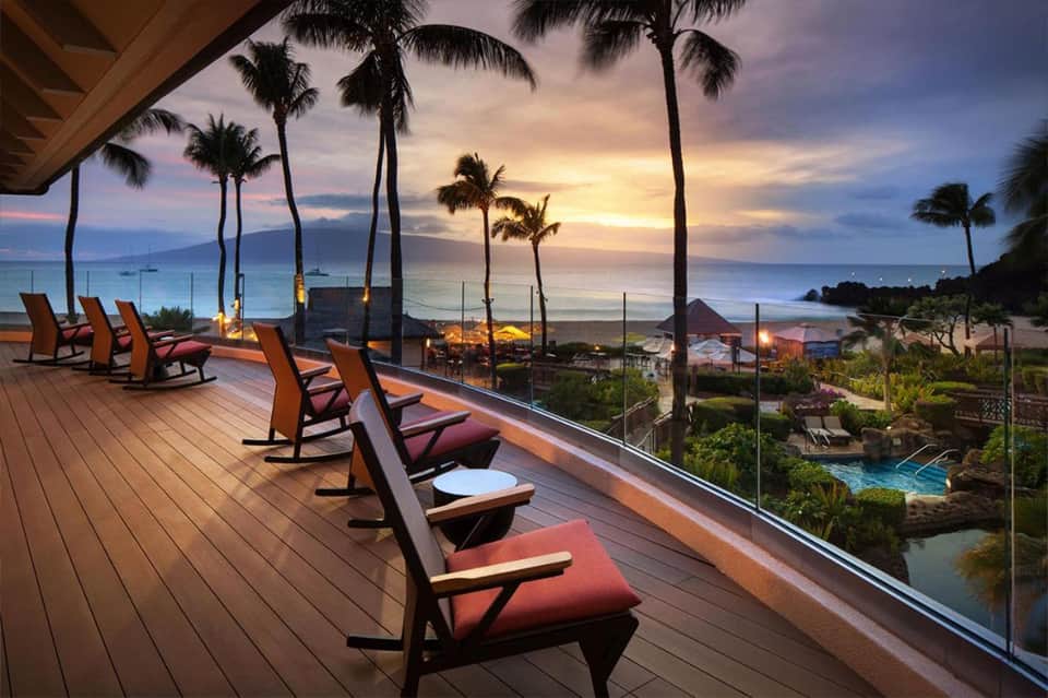 Beachfront sunset terrace with lounge chairs, palm trees, and ocean view