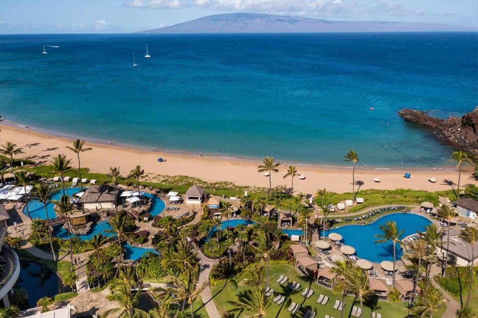 Aerial view of tropical beach resort with multiple blue pools, palm trees, and turquoise ocean