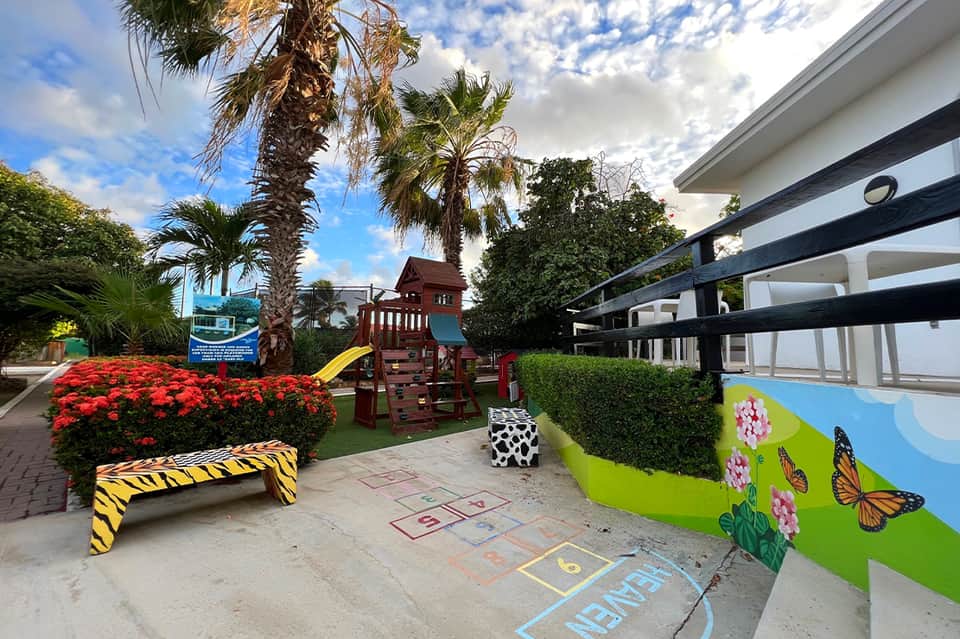 Children's play area with colorful playground equipment, flower mural, and palm trees