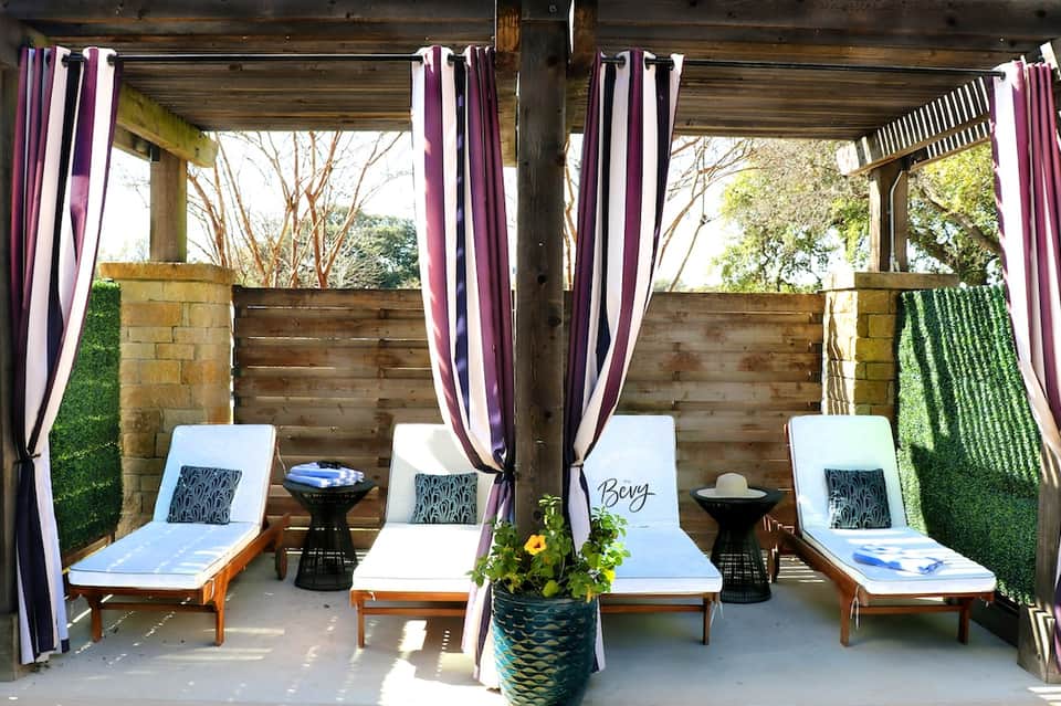 Indoor spa cabanas with purple striped curtains, lounge chairs, side tables, and ambient lighting