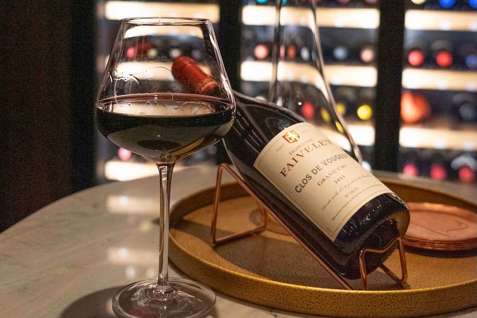 Glass of red wine with a bottle on a wooden tray in a wine cellar with blurred wine racks