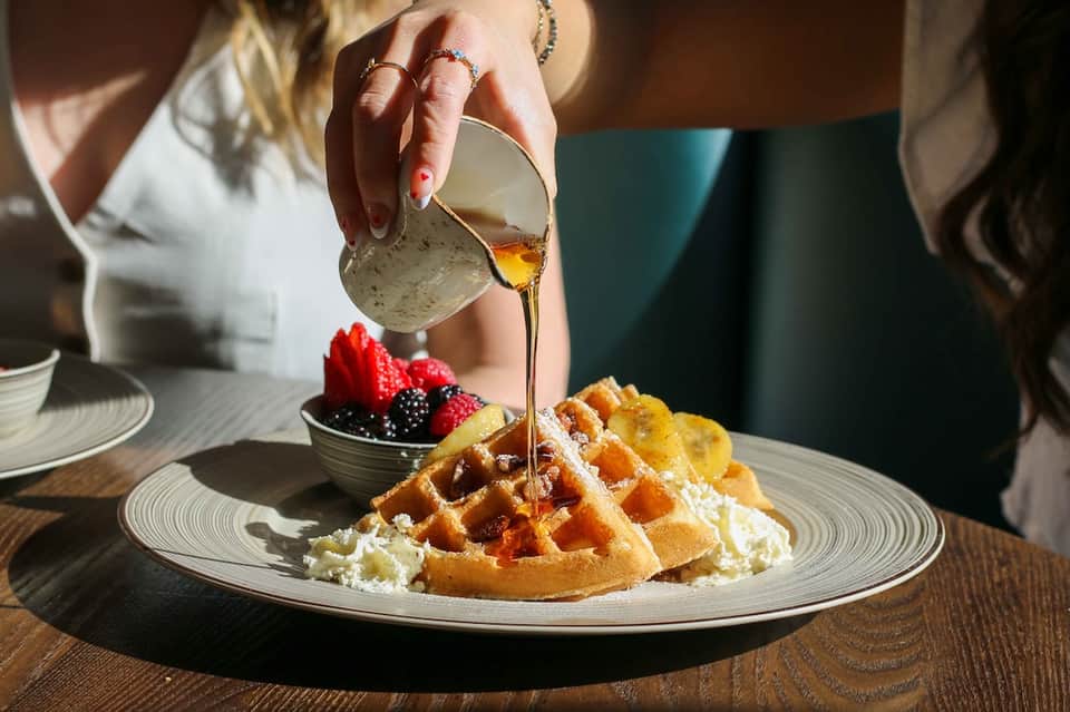 Close-up of gourmet waffles with whipped cream and berries being drizzled with honey sauce at fine dining