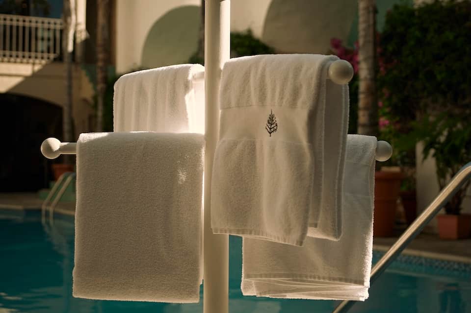 White embroidered resort towels hanging on rail overlooking poolside patio and greenery