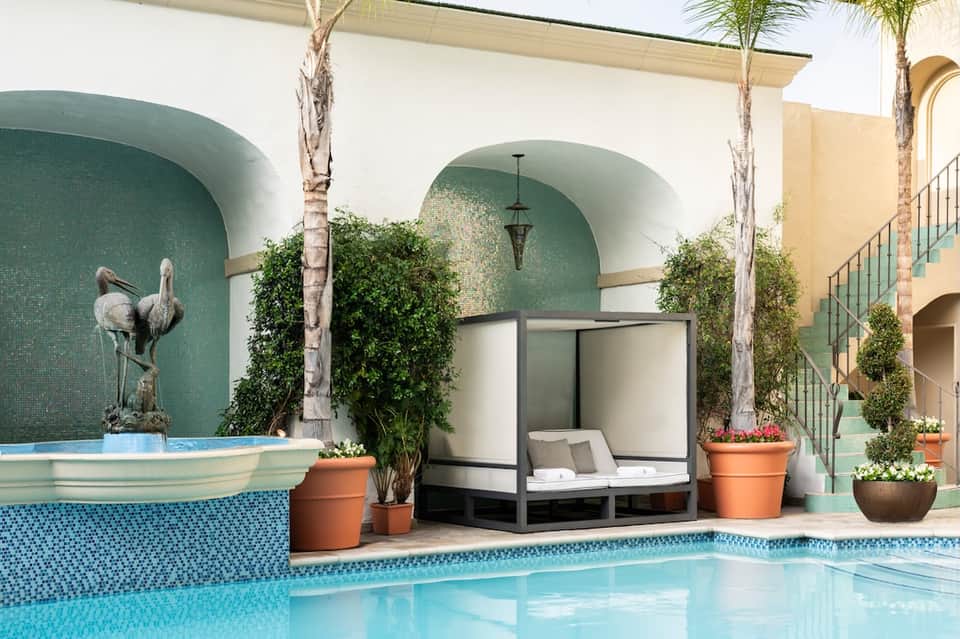 Mediterranean courtyard pool with arched alcoves, turquoise tile, and tropical landscaping