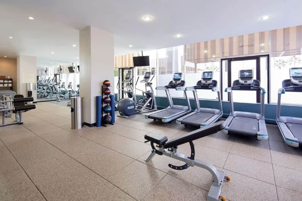 Bright fitness center with treadmills, exercise bikes, and floor-to-ceiling windows