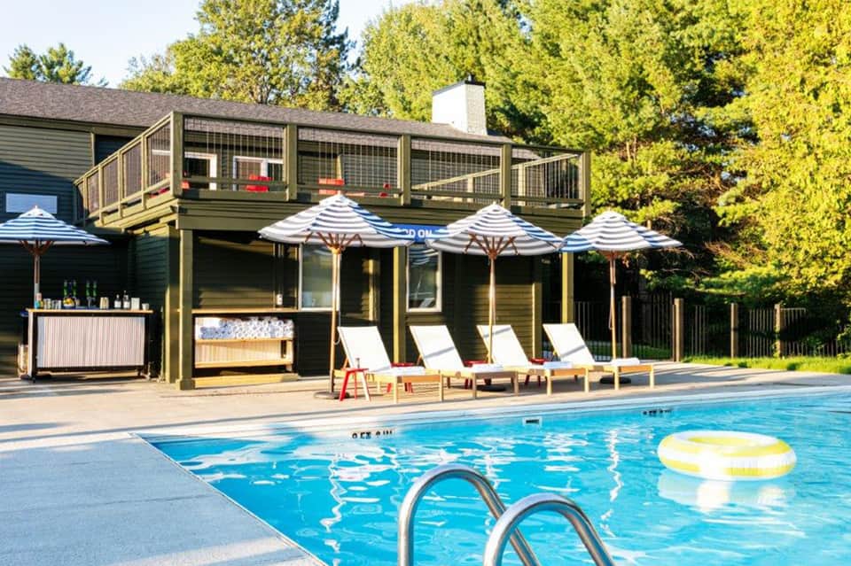 Residential pool area with striped umbrellas, lounge chairs, and modern deck house