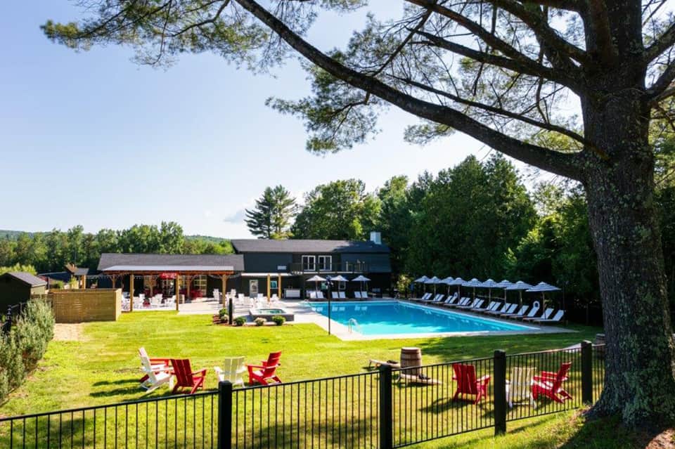 Resort pool surrounded by green lawn, red Adirondack chairs, and main lodge building under trees