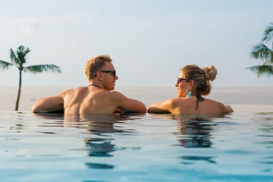 Couple relaxing in infinity pool overlooking ocean with palm trees on horizon