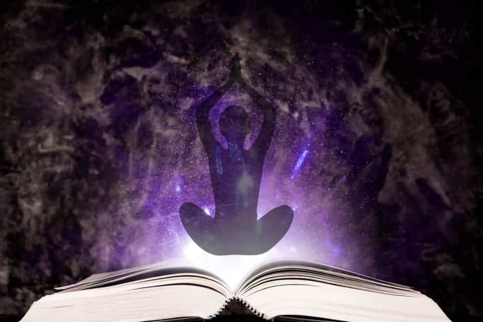 Silhouette of meditating figure glowing in purple light rising from open book