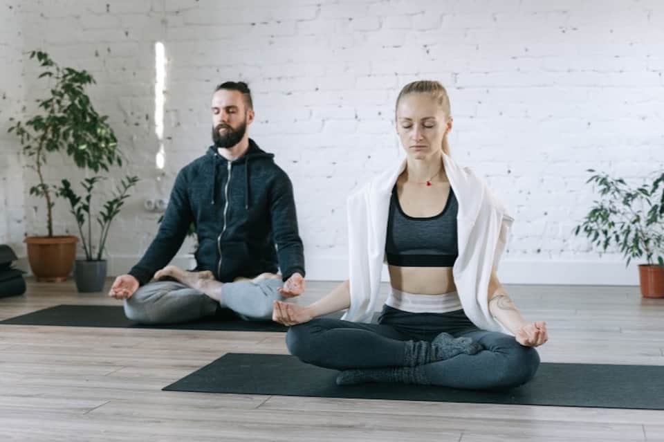 Two people meditating in a bright yoga studio with potted plants