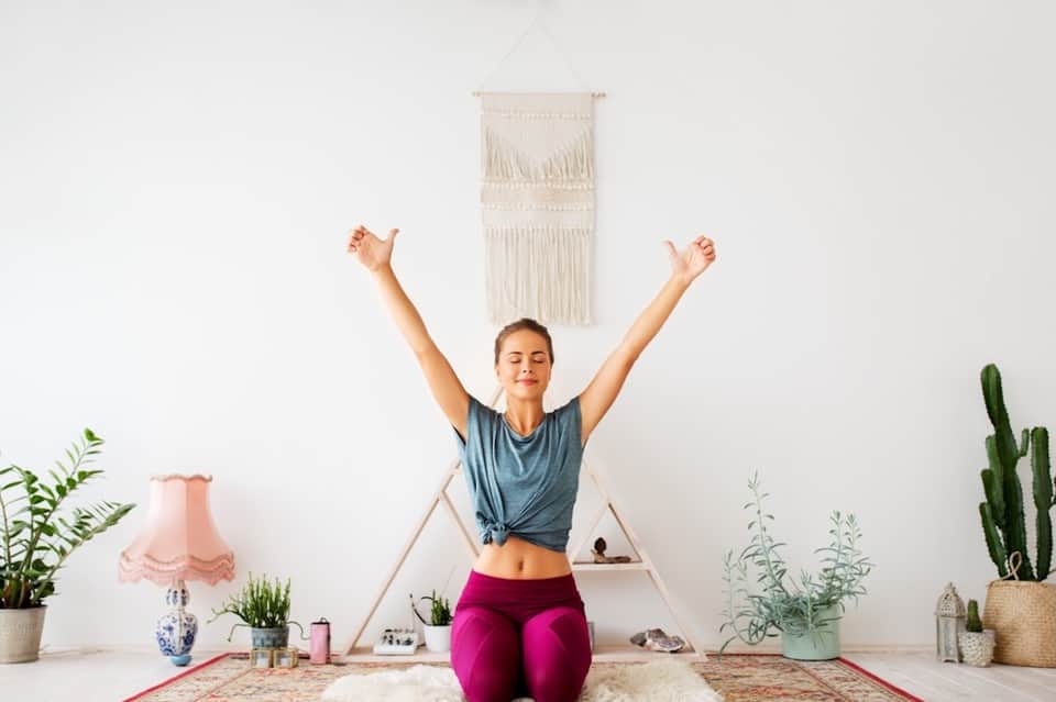 Woman in yoga pose celebrating in minimalist bedroom with macramé wall hanging