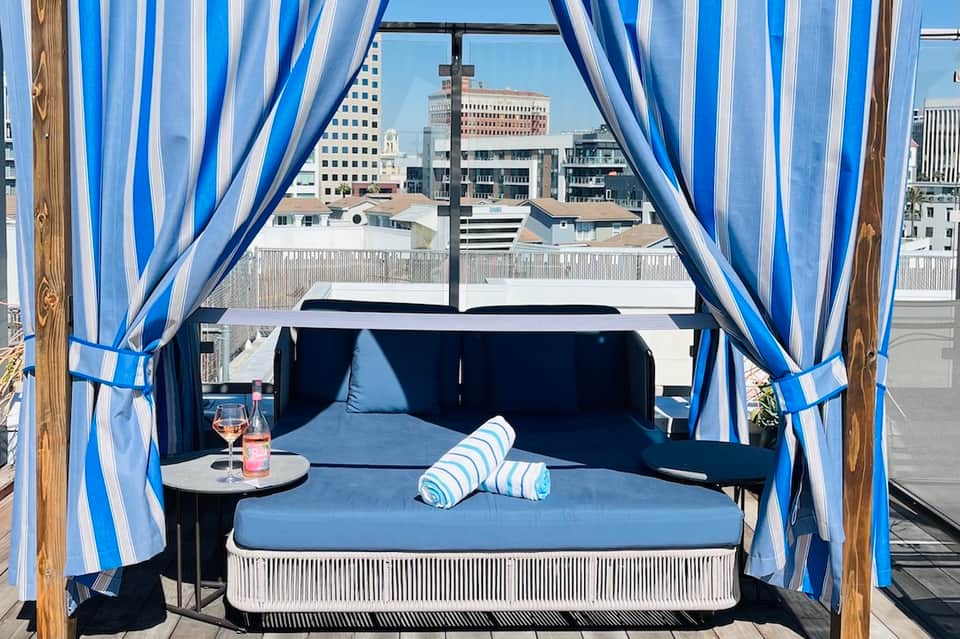 Rooftop cabana with blue and white striped curtains, daybed, and city skyline view