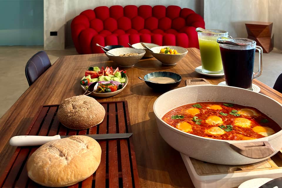 Dining table with bread, soup bowls, salads, and beverages against red modern sofa
