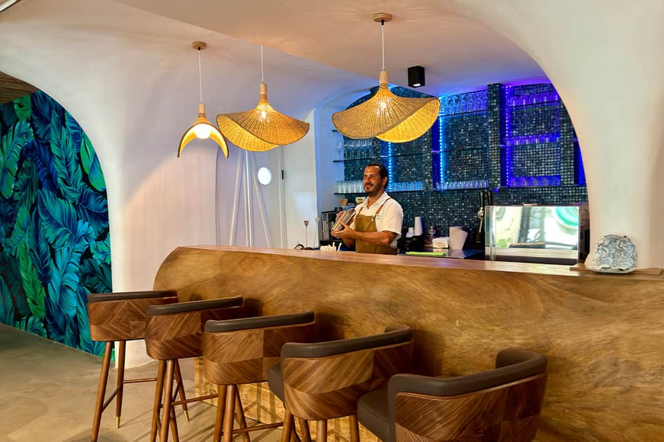 Modern hotel bar with curved wooden counter, golden pendant lights, and city skyline view