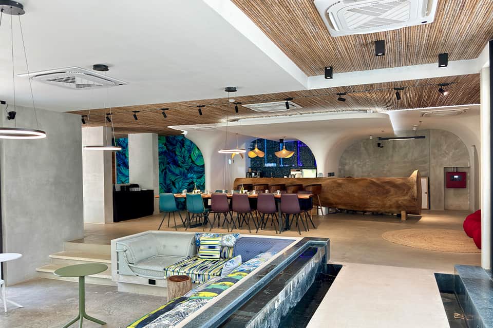 Modern hotel common area with wooden ceiling, dining tables, bar, and contemporary furnishings