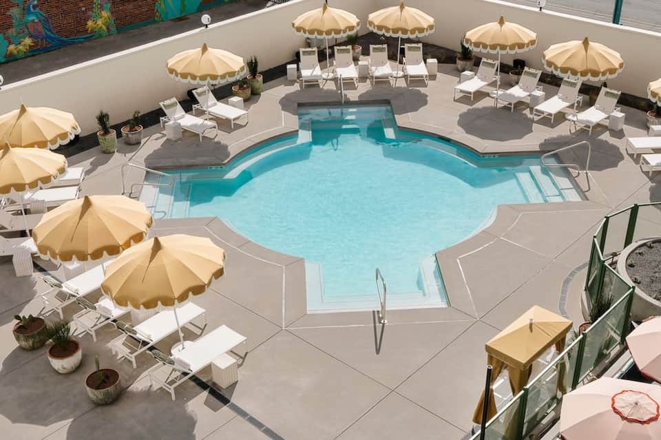 Curved turquoise pool surrounded by cream umbrellas, white lounge chairs, and white perimeter walls