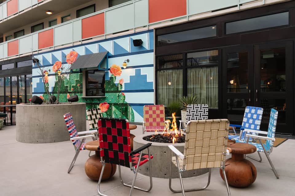 Colorful outdoor patio with firepit, vibrant patterned chairs, cactus planter, and building backdrop