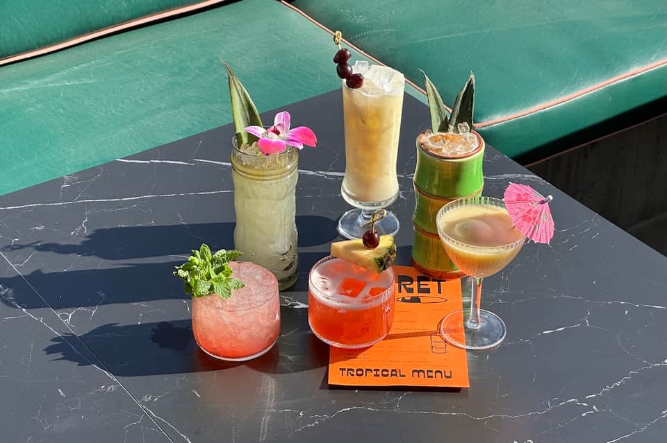 Tropical cocktails on black marble table with pool in background