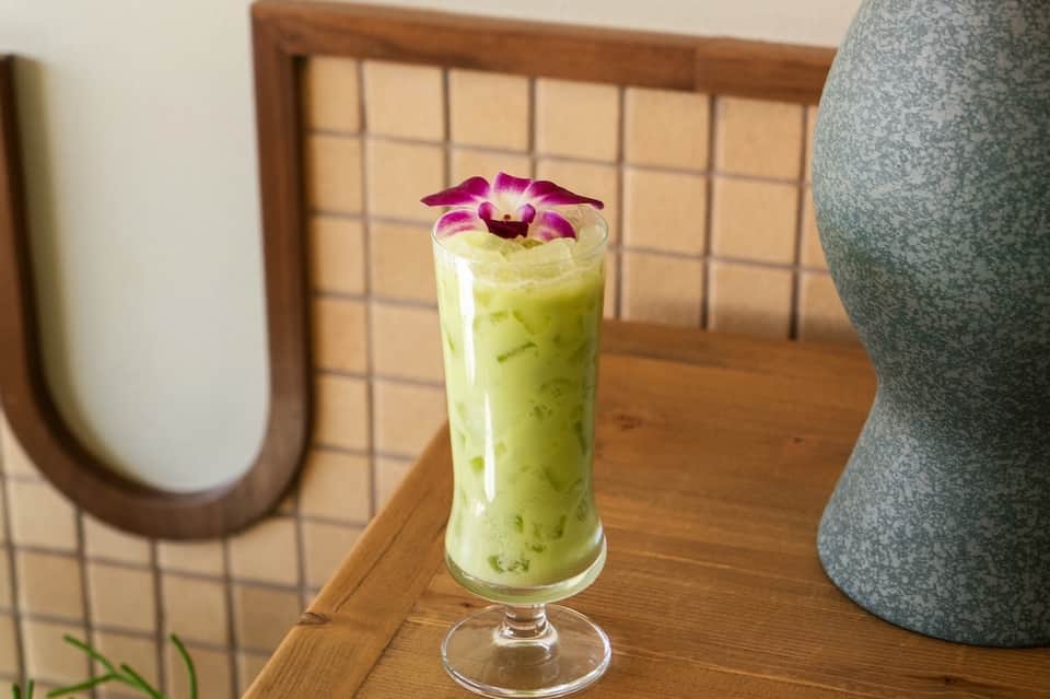 Green matcha beverage in tall glass garnished with purple orchid flower