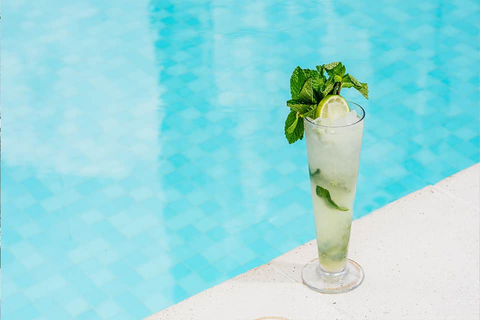 Refreshing mojito cocktail with mint and lime on pool deck overlooking turquoise water