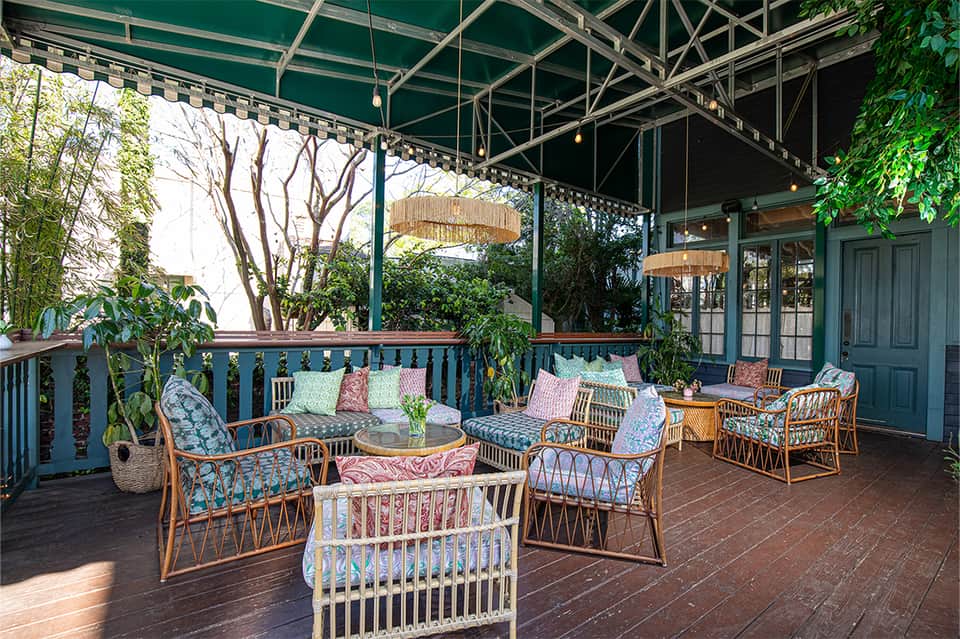 Covered resort patio with wicker lounge chairs, colorful cushions, climbing vines, and lush greenery