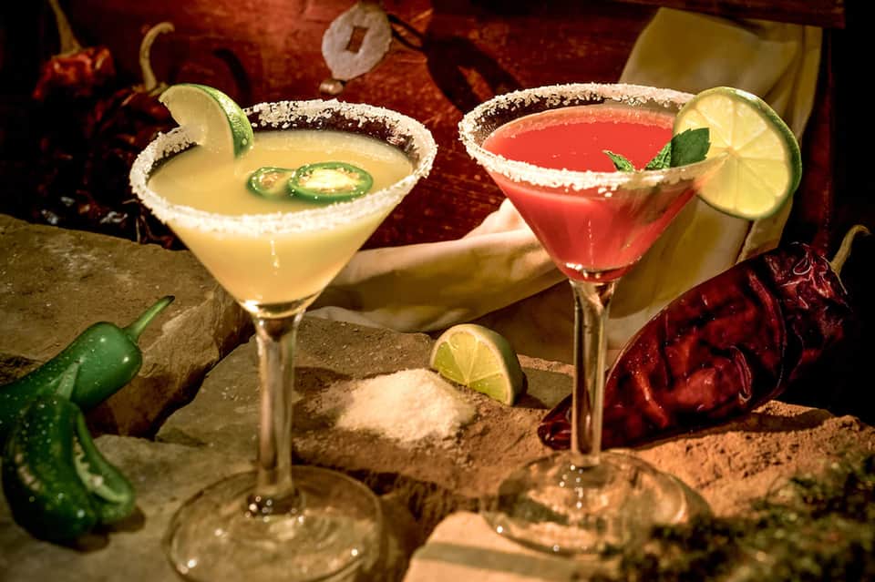 Two margarita cocktails with salt-rimmed glasses, lime garnish, and jalapeño slices