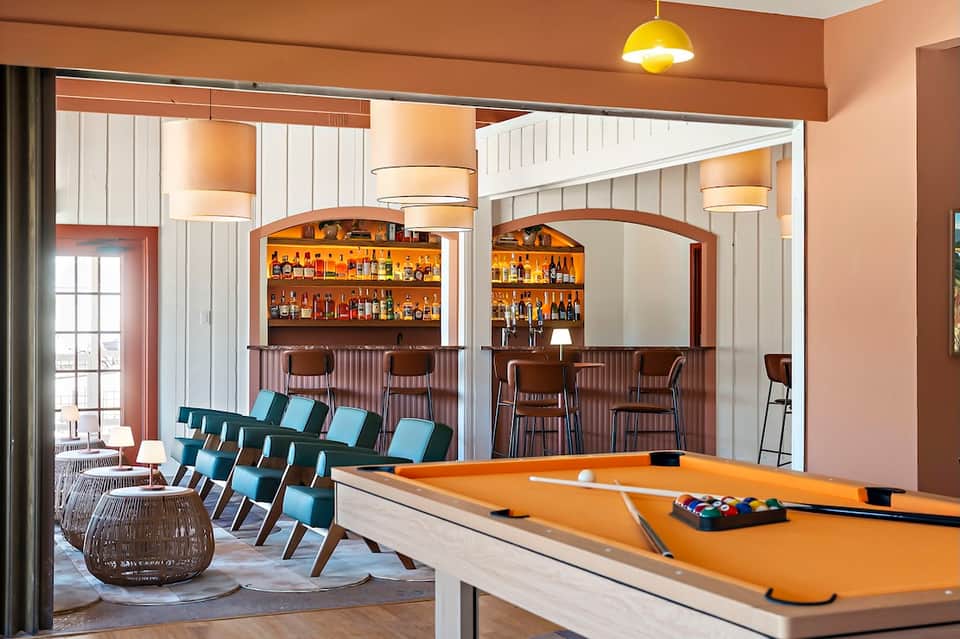 Hotel recreation room with billiards table, bar area with stocked shelves, and lounge seating
