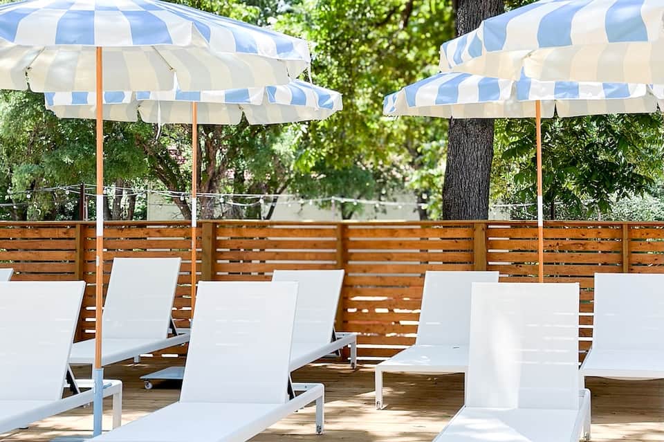 Outdoor seating area with striped umbrellas and wooden privacy fence