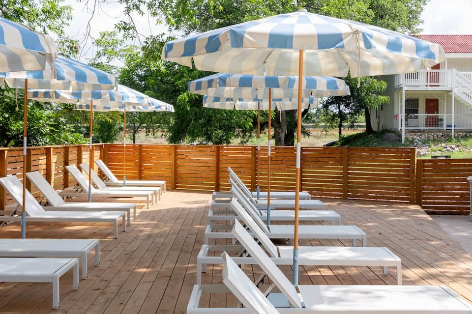 Outdoor deck lounge with white loungers, blue and white striped umbrellas, and wooden privacy screens