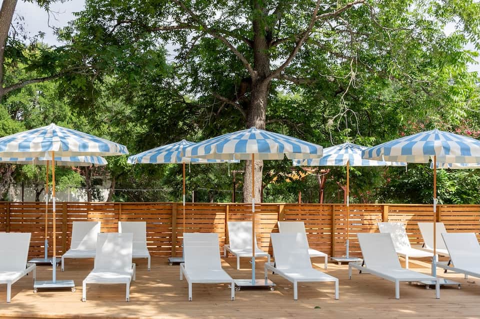 Outdoor lounge area with striped umbrellas and white loungers under trees