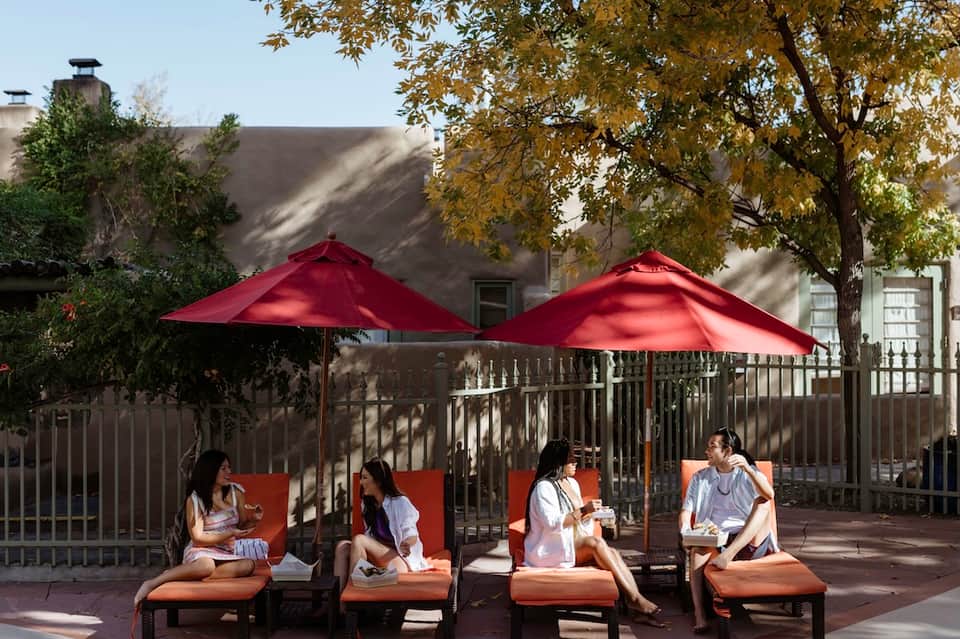 Terrace seating under cream umbrellas beside green-tinted swimming pool with landscape views