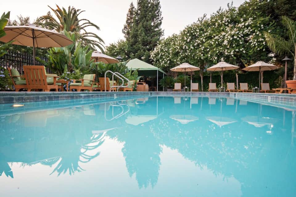 Large outdoor pool with clear blue water, palm trees, lounge chairs, and umbrellas for shade