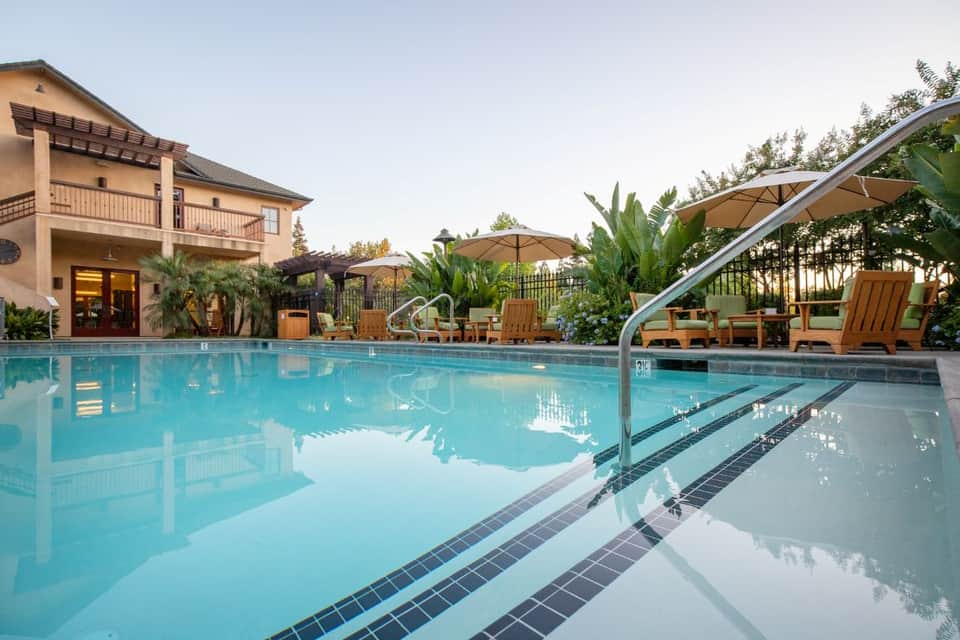 Resort swimming pool at dusk with lounge chairs, umbrellas, and illuminated building entrance
