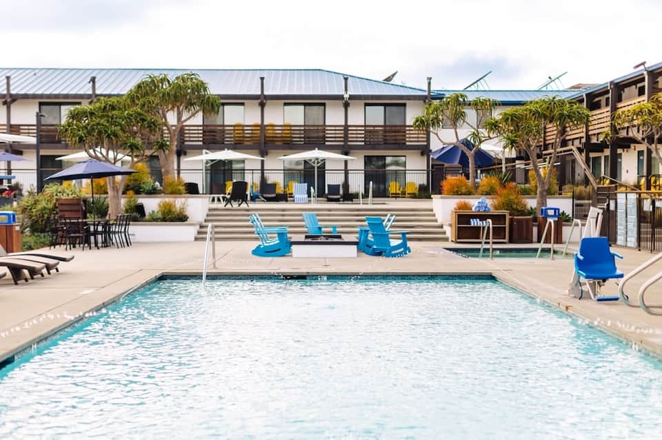 Resort pool with blue Adirondack chairs, cabanas, and modern lodge-style building