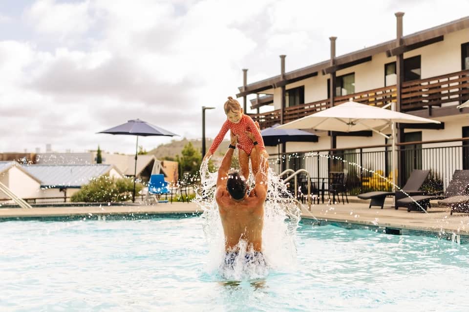 Child splashing in resort pool with modern architecture and umbrellas in background