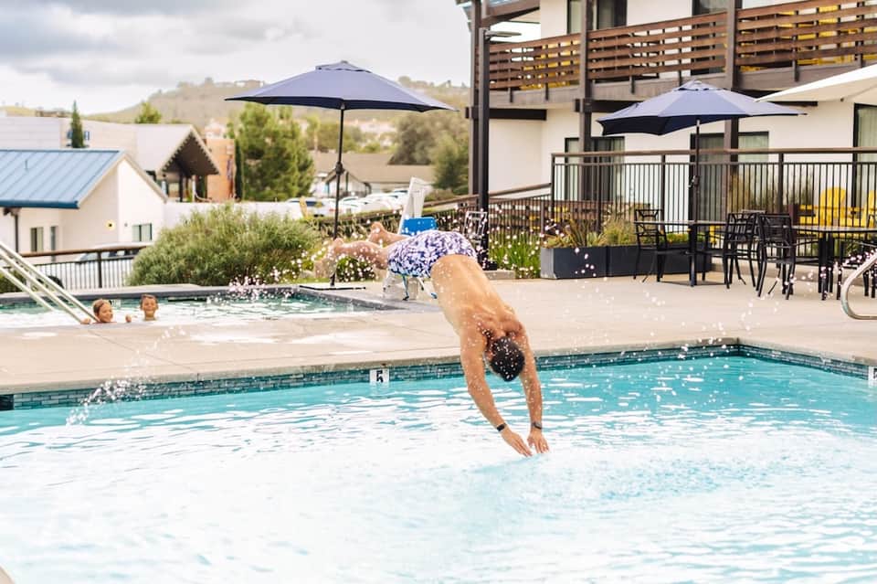 Guest diving into outdoor swimming pool with hot tub, umbrellas, and hillside resort views
