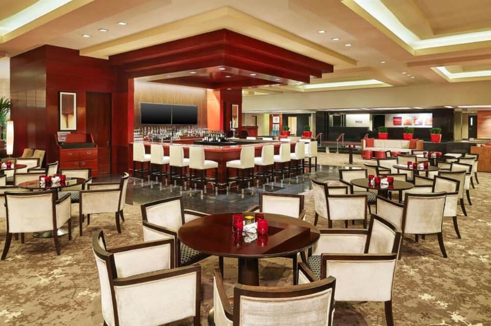 Elegant hotel lounge with red accent walls, bar seating, and cream armchairs