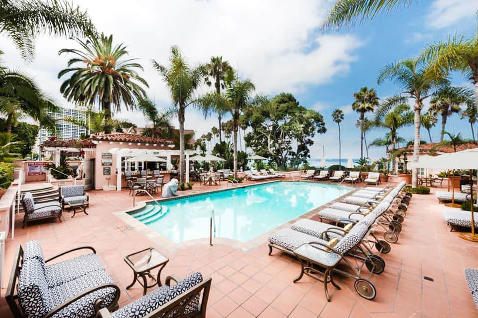 Oceanfront resort pool with terracotta patio, loungers, palm trees, and pink cabana building under blue sky