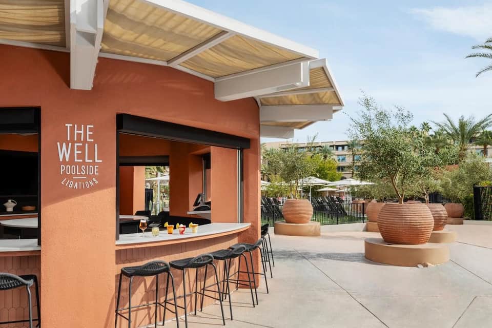 Orange poolside bar structure with wooden pergola roof, seating, and large terracotta planters